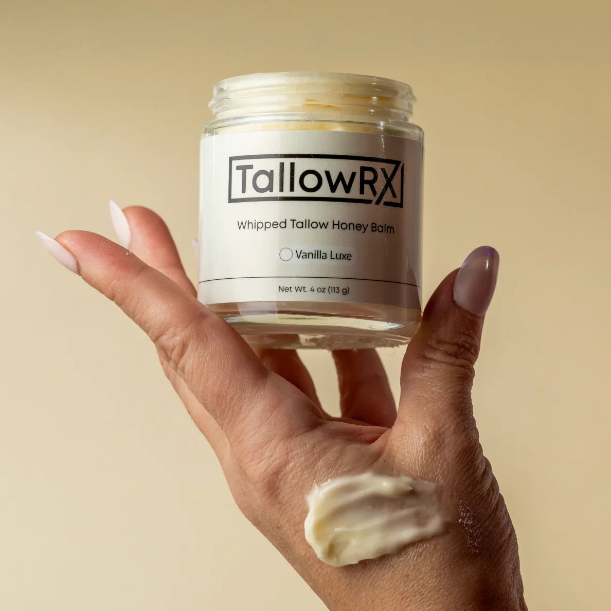 Hand holding TallowRX Vanilla Luxe whipped tallow balm with a swipe of creamy moisturizer applied to skin, 4 oz glass jar